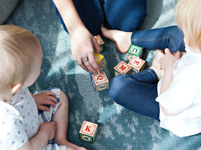 Enfant jouant avec des cubes en bois accompagné par sa nounou